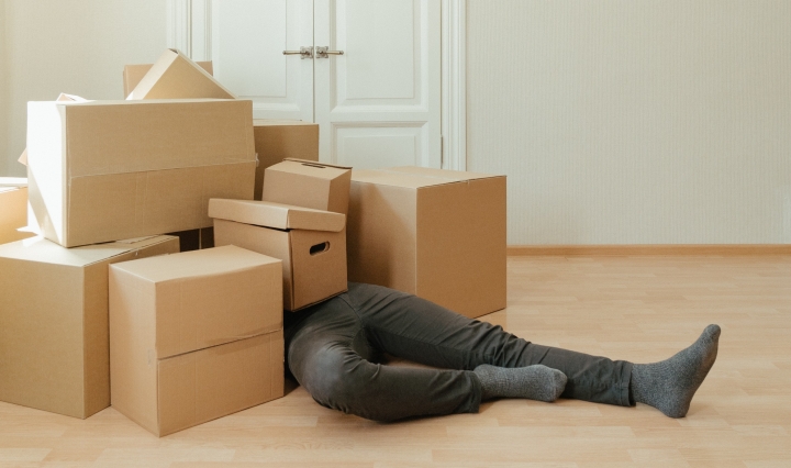 An image of a pile of boxes with a man underneath them.