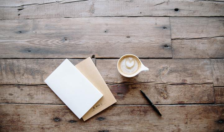 An image of a cup of coffee and two notebooks on a wooden table.