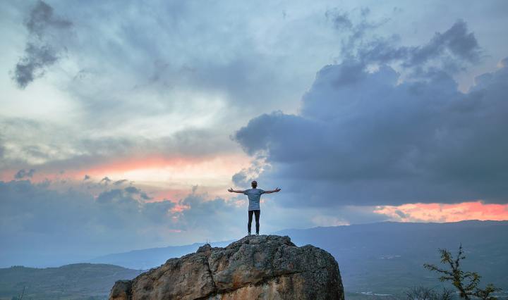 An image of a man on a cliff, holding out his arms to the sky.